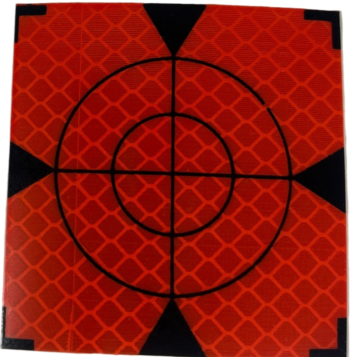 Small square target with concentric circles and a crosshair on an orange background, placed on a white surface.